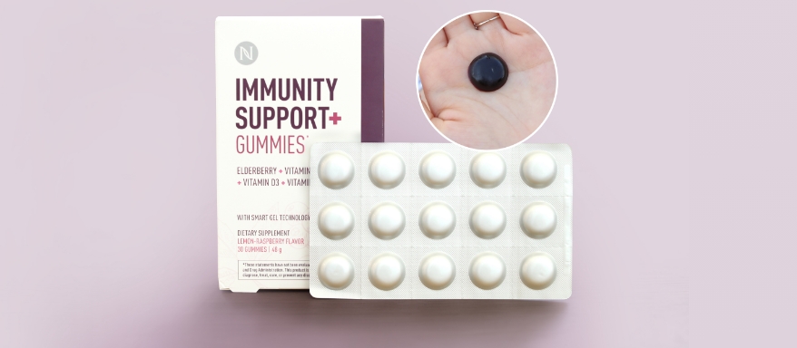 Image of a close-up of an Immunity Support + Gummy with the product packaging and carton on a light pink background.